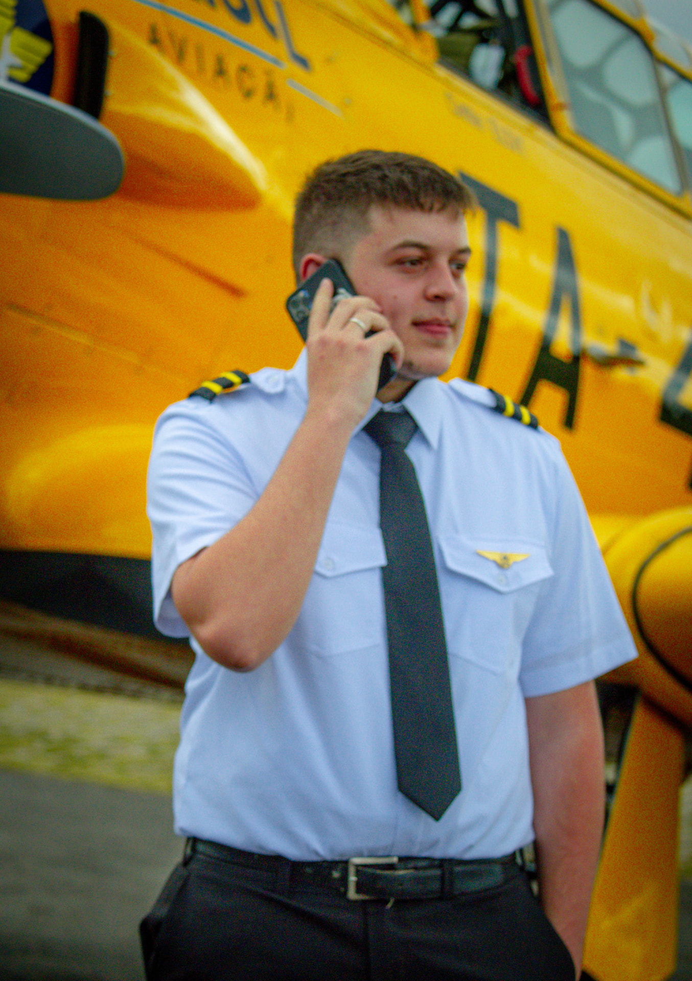 Lucas Desplanches de uniforme de piloto, ao telefone ao lado de uma aeronave